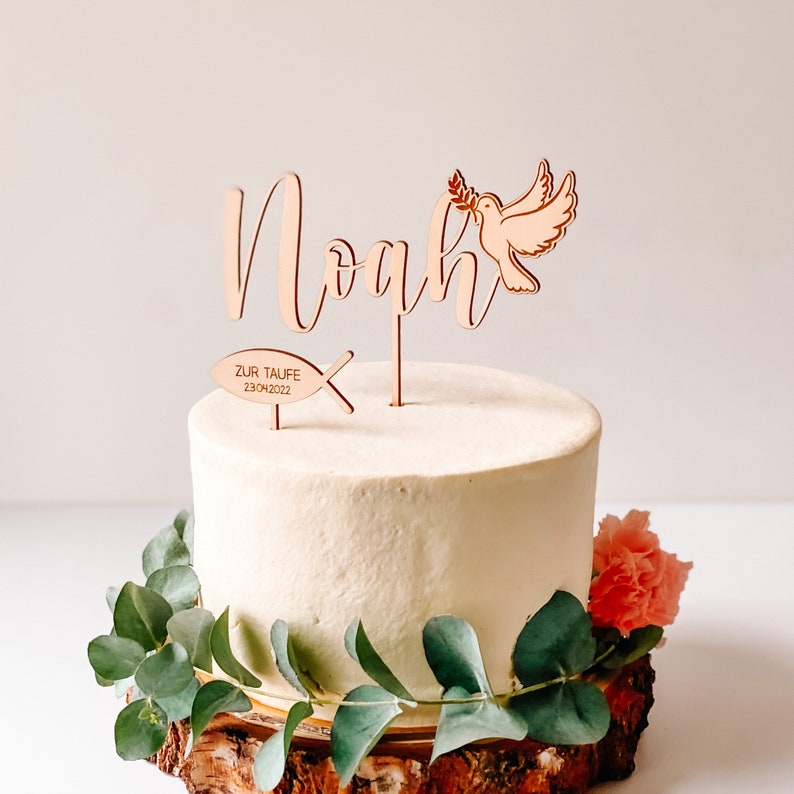 May include: Wooden cake topper with the name Noah, a dove with an olive branch, and a fish with the text "Zur Taufe 23.04.2022".