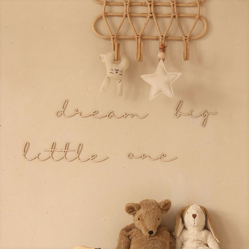 May include: A nursery wall decor set with the words "dream big little one" in cursive script. The set includes a wooden star, a bunny, and a rattan wall hanging with hooks.