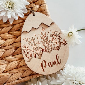 May include: A wooden egg-shaped ornament with a floral design and the name "Paul" engraved on it. The ornament is made of light brown wood and has a delicate floral pattern.