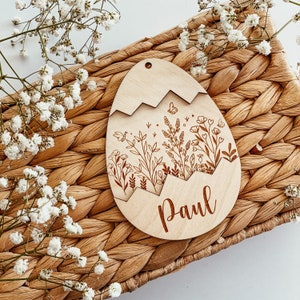 May include: A wooden egg-shaped ornament with a floral design and the name "Paul" engraved on the bottom. The ornament is light brown and has a delicate, intricate design.