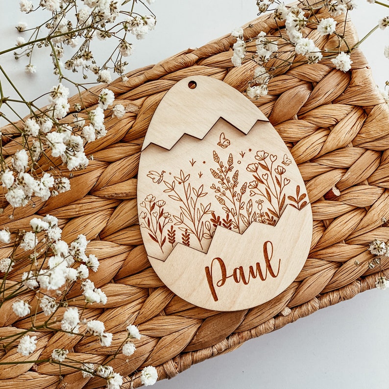 May include: A wooden egg-shaped ornament with a floral design and the name "Paul" engraved on the bottom. The ornament is light brown and has a delicate, intricate design.