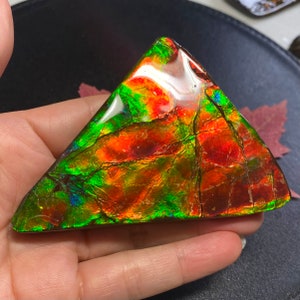 May include: A triangular piece of iridescent ammolite with a green, red, and orange color pattern.