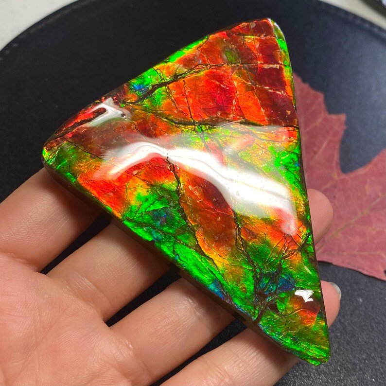 May include: A triangular piece of iridescent opal with red, green, and blue hues. The opal is polished and has a smooth surface.