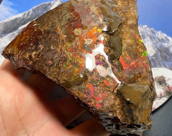 May include: A large, rough, iridescent, multi-colored, natural opal stone with a brown, gray, and black matrix. The opal displays a rainbow of colors, including red, orange, yellow, green, blue, and purple.