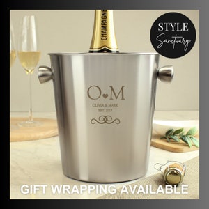 Peut inclure: Un seau à champagne en argent avec une inscription personnalisée "O.M Olivia & Mark Est. 2017" et une bouteille de champagne à l'intérieur. Le seau a deux poignées sur les côtés.