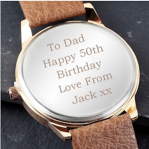 May include: A gold-tone watch with a brown leather band. The watch face is engraved with the message "To Dad Happy 50th Birthday Love From Jack xx".