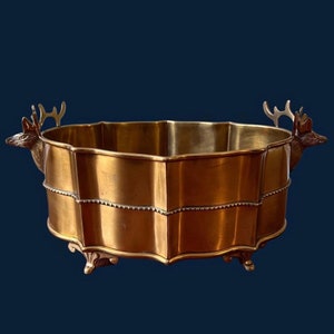 May include: A gold-toned metal planter with a scalloped edge and deer head handles. The planter has a beaded trim around the top edge.