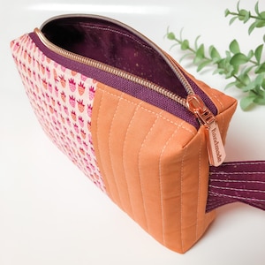 May include: A quilted orange and pink fabric zippered pouch with a pink and white strawberry print on one side. The zipper pull has a copper finish and says "Handmade".
