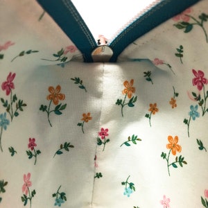 May include: A teal zipper runs along the top of a white fabric pouch with a small floral pattern. The zipper is open, revealing the inside of the pouch.