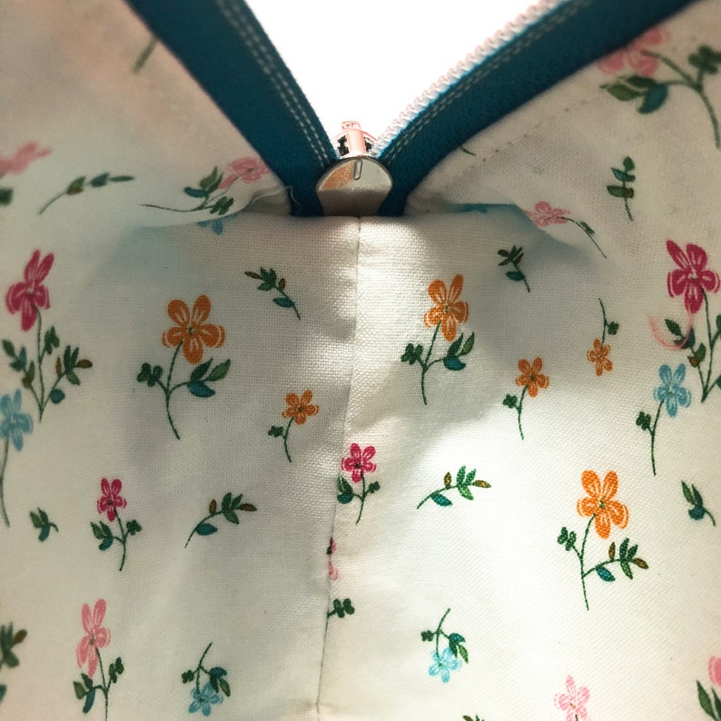 May include: A teal zipper runs along the top of a white fabric pouch with a small floral pattern. The zipper is open, revealing the inside of the pouch.
