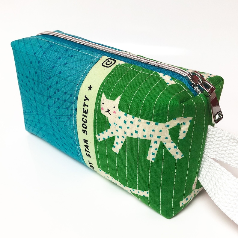 May include: A turquoise and green zippered pouch with a white cat illustration and the text "By Star Society" on the side. The pouch has a white zipper pull.