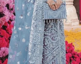 Puede incluir: Un vestido formal bordado en azul claro con bufanda y bolso a juego. El vestido presenta detalles y adornos intrincados. El fondo incluye flores rosas y un suelo floral amarillo.