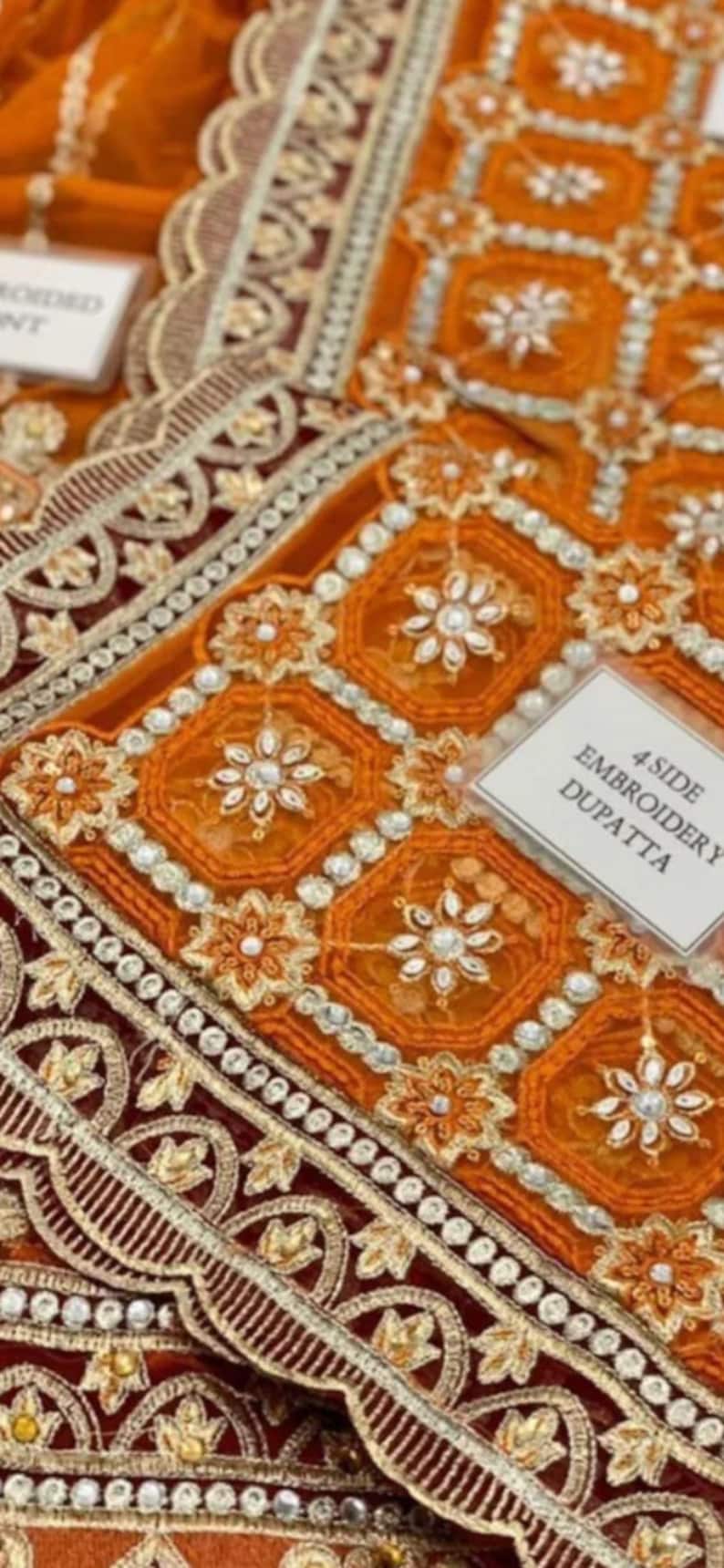 May include: Orange and maroon embroidered fabric with a scalloped edge and a label that reads "4 Side Embroidery Dupatta".