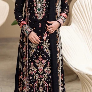 May include: A black embroidered dress with floral patterns and a matching black dupatta. The dress has a long sleeve and a high neckline. The dupatta has a white lace trim.