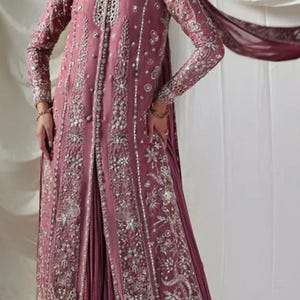 May include: A mauve-colored formal dress with intricate silver embroidery. The long-sleeved dress features a high neckline and a flowing skirt. A matching scarf drapes over the shoulder. The dress is suitable for special occasions.