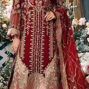 May include: A maroon and gold embroidered dress with a matching dupatta. The dress has a long, flowing skirt with a ruffled hem and a fitted bodice with a deep neckline. The dupatta is sheer and has a delicate floral pattern.