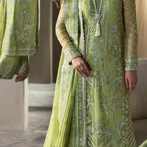 May include: A light green embroidered formal outfit. The ensemble includes a long-sleeved tunic, matching pants, and a sheer scarf. The outfit features intricate silver embroidery and embellishments.