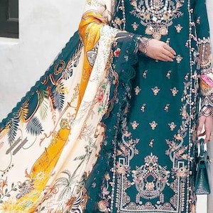 May include: A teal embroidered dress with intricate floral and geometric patterns. The dress features long sleeves and a matching scarf with a vibrant print of flowers, palm trees, and zebra stripes. A small teal handbag completes the ensemble.