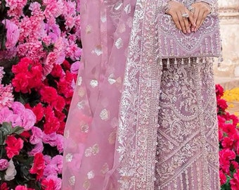 Könnte beinhalten: Ein formelles Outfit in Lavendelfarbe mit aufwendiger Silberstickerei. Das Ensemble umfasst ein langärmliges Oberteil, einen passenden Rock und einen transparenten Schal. Das Outfit wird mit einer kleinen passenden Handtasche ergänzt. Der Hintergrund zeigt leuchtend rosa und rote Blumen.