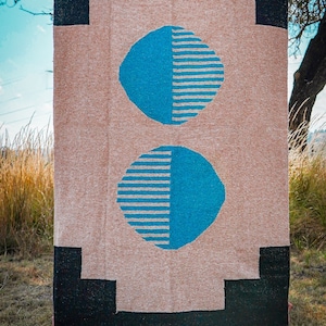 May include: A woven rug with a beige background and black border. Two large blue circles with white stripes are centered on the rug.