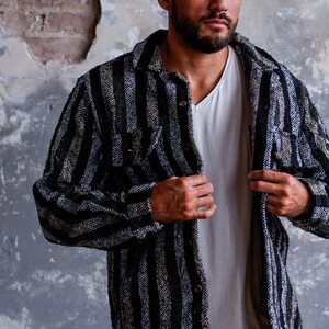 May include: A black and gray striped shirt jacket with a button-down front and two chest pockets. The jacket is worn over a white V-neck shirt. The fabric has a textured appearance.