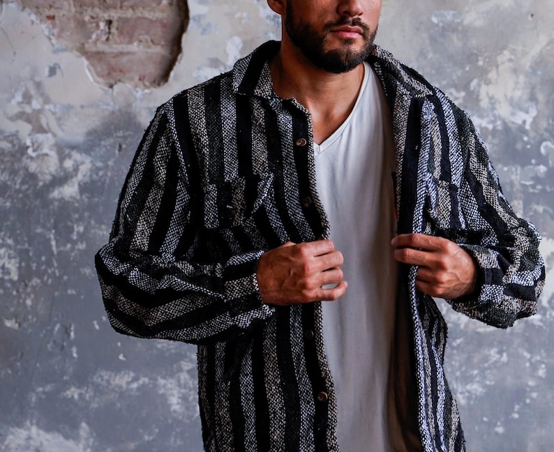 May include: A black and gray striped shirt jacket with a button-down front and two chest pockets. The jacket is worn over a white V-neck shirt. The fabric has a textured appearance.