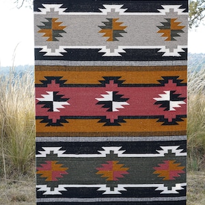 May include: A colorful woven rug with a geometric pattern in shades of black, white, red, orange, and green. The rug has a traditional southwestern style.
