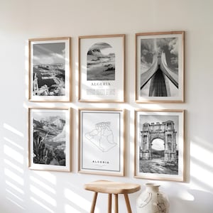 Peut inclure: Six cadres en noir et blanc avec des cadres en bois sont exposés sur un mur blanc. Les tirages présentent des paysages, de l'architecture et une carte de l'Algérie. Le mot "ALGERIA" est imprimé sur deux des tirages.