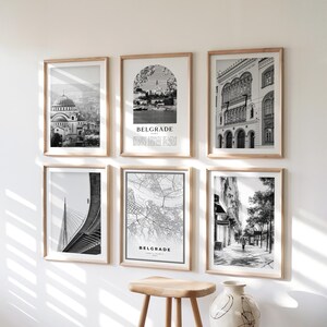 May include: A collection of six framed black and white prints. The prints depict architectural scenes, cityscapes, and a map, all with a focus on Belgrade. The frames are a light wood color, and the prints are displayed on a white wall.