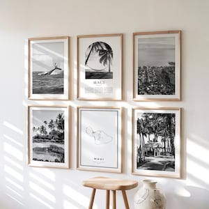 Puede incluir: Seis impresiones en blanco y negro enmarcadas de paisajes de Maui. Las impresiones presentan imágenes de una ballena saltando, palmeras, un mapa y escenas costeras. Los marcos son de madera de color claro.