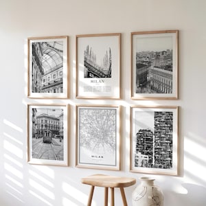 May include: Six framed black and white prints of Milan, Italy, hang on a white wall. The prints depict architectural details, cityscapes, and a map of the city. The frames are made of light-colored wood, and the overall aesthetic is modern and minimalist.
