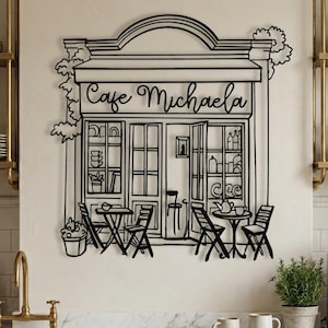 Personalized black metal cafe sign with "Cafe Michaela" script text hanging in a modern farmhouse kitchen.