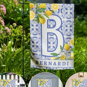 Op de afbeelding: Een tuinvaandel met een blauw en wit tegelpatroon, met een grote letter "B" en citroenillustraties. De naam "BERNARDI" staat onderaan gedrukt. De vlag wordt getoond op een zwarte metalen standaard in een tuin.