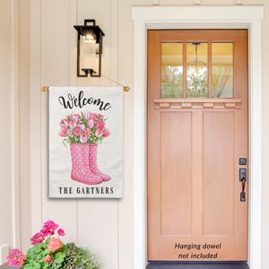 May include: Welcome sign with pink rain boots and pink flowers. The sign says "Welcome The Gartners".