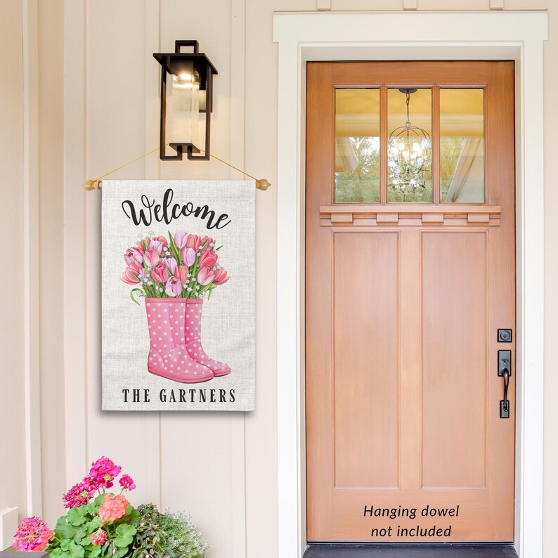 May include: Welcome sign with pink rain boots and pink flowers. The sign says "Welcome The Gartners".