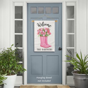 May include: A welcome sign with a pink and white floral design. The sign features a bouquet of pink tulips in a pair of pink rain boots with white polka dots. The text "Welcome The Gartners" is printed on the sign.