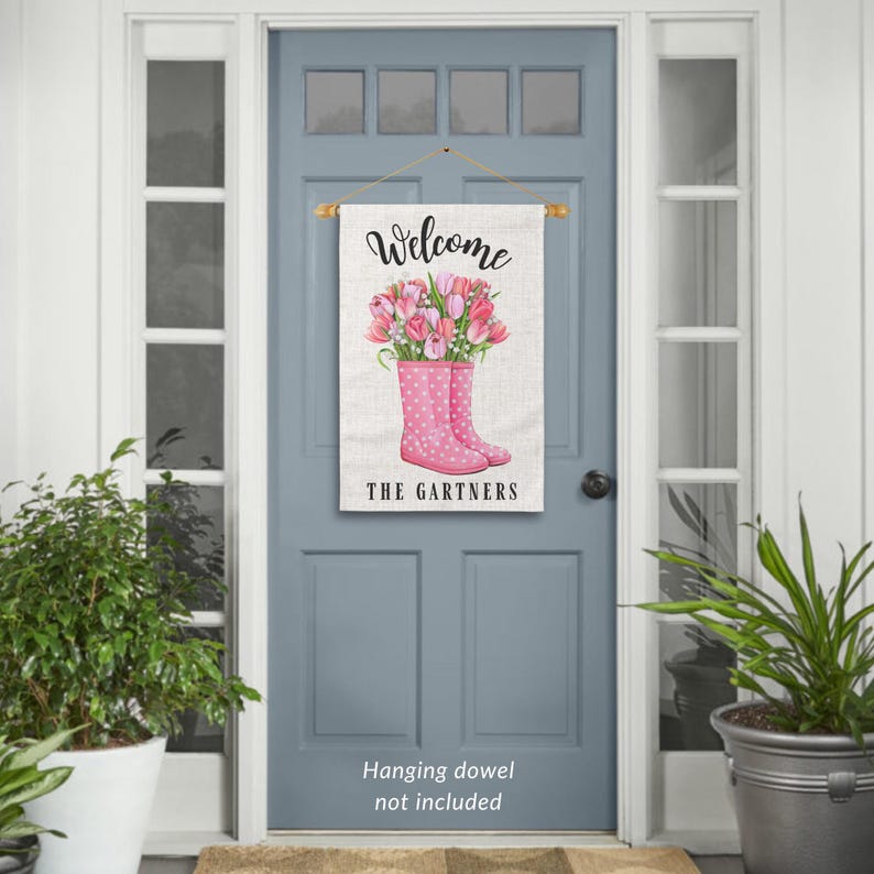 May include: A welcome sign with a pink and white floral design. The sign features a bouquet of pink tulips in a pair of pink rain boots with white polka dots. The text "Welcome The Gartners" is printed on the sign.