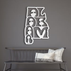 Puede incluir: Una pieza de arte mural de metal blanco que deletrea "ALABAMA" en una fuente estilizada. La obra de arte est&aacute; montada en una pared gris sobre un banco gris oscuro con almohadas.