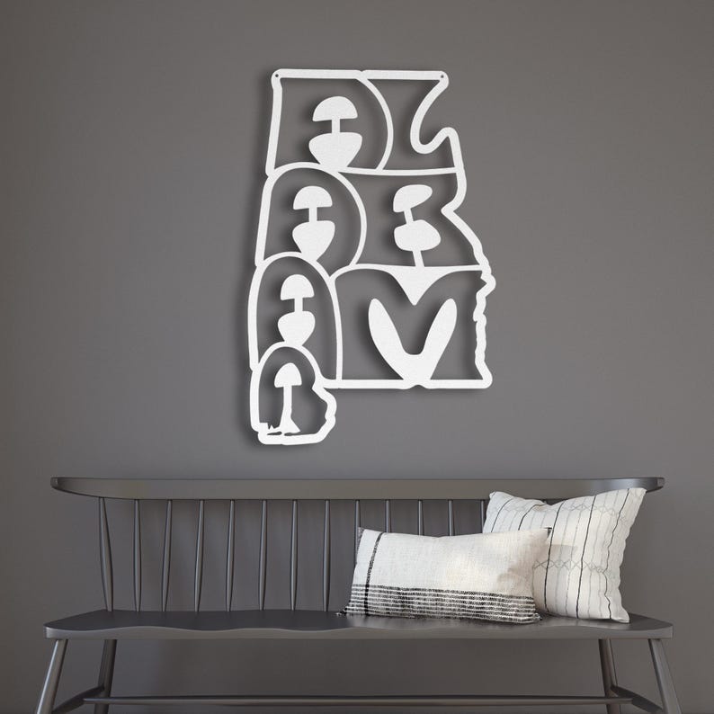 Puede incluir: Una pieza de arte mural de metal blanco que deletrea "ALABAMA" en una fuente estilizada. La obra de arte est&aacute; montada en una pared gris sobre un banco gris oscuro con almohadas.