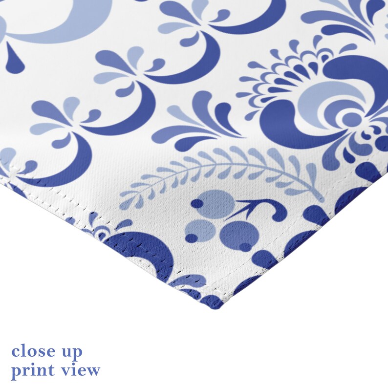 May include: Close-up of a white fabric with a blue and white floral pattern. The fabric has a stitched edge.