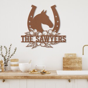 May include: A brown metal wall art piece featuring a horse head inside a horseshoe, with floral accents and the text "THE SAWYERS". The artwork is likely for home decor, possibly for a family with a love for horses.