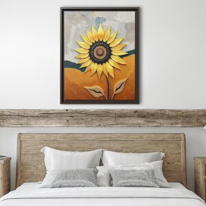 Puede incluir: Una obra de arte en lienzo enmarcada con un girasol texturizado. El girasol tiene p&eacute;talos amarillos y un centro marr&oacute;n oscuro. El fondo tiene tonos de naranja, verde y gris. La obra de arte se exhibe sobre un cabecero de madera.
