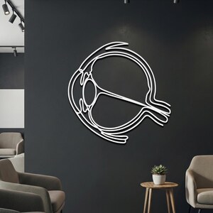 White medical science line art on dark wall showing cross-section of cornea, lens, and optic nerve.