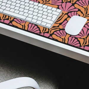 May include: A black and orange desk mat with a pink and orange floral pattern. A white keyboard and mouse are on the mat.