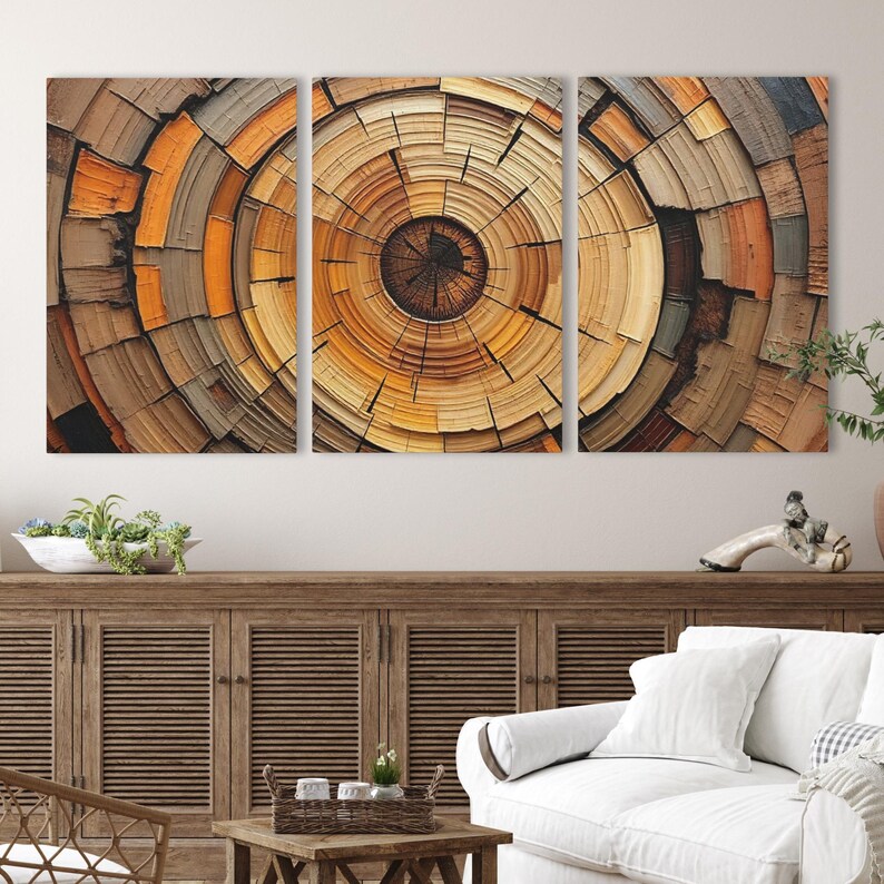 May include: A triptych of abstract art panels featuring a concentric circular design reminiscent of tree rings. The artwork showcases a range of warm, earthy tones, including browns, oranges, and yellows, creating a natural and textured appearance. The panels are mounted on a wall.