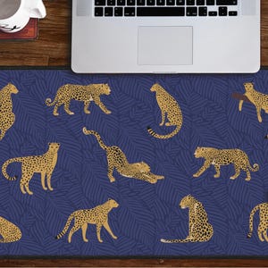 May include: A blue and gold mouse pad with a repeating pattern of leopards on a leafy background. The mouse pad is designed for use with a computer mouse.