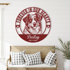 May include: A burgundy metal wall art piece featuring a dog's portrait within a circular frame. The text "FOREVER IN OUR HEARTS" encircles the dog, with the name "Bailey" and dates "2011-2025" below. Two paw prints are on either side.