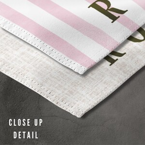 May include: Close-up detail of a white and pink striped fabric with a stitched edge. The fabric has the word "ROOM" printed in brown letters.