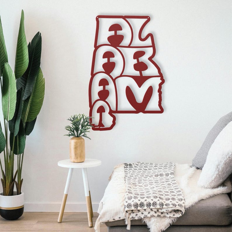 Puede incluir: Una pieza de arte mural de metal rojo que deletrea "ALABAMA" en una fuente estilizada. La obra de arte est&aacute; montada en una pared blanca, con un sof&aacute; y plantas en el fondo. La pieza mide aproximadamente 61 cm de ancho y 91 cm de alto.