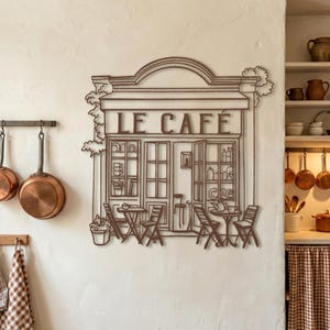 Rust copper patina metal coffee shop sign reading "Le Cafe" on a textured plaster wall with hanging copper pots.
